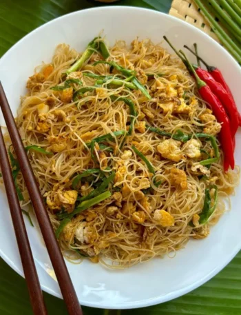 A plate of pad mee garnished with green onions and red chilies, ready to be eaten with wooden chopsticks.