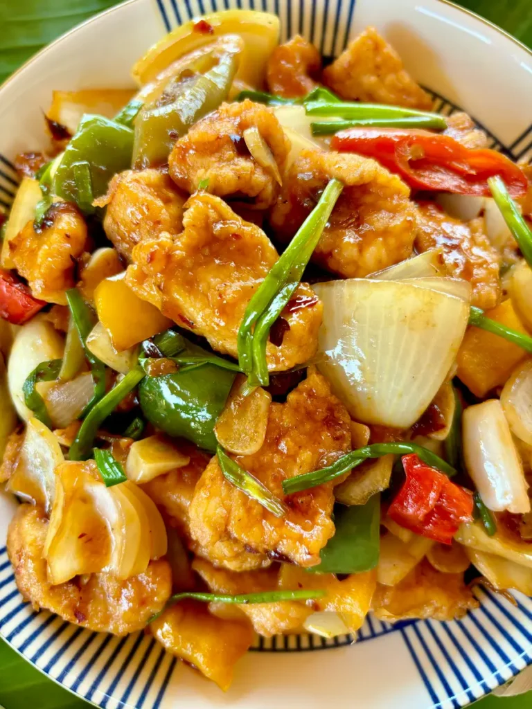 Close-up of pad prik pao chicken with crisp vegetables like bell peppers and onions, drenched in a spicy sauce.