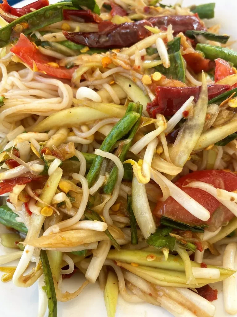 Close-up of spicy Thai papaya salad with vermicelli noodles, tomatoes, green beans, and chilies.