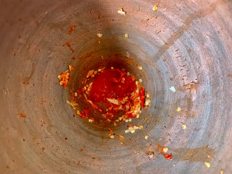 Chilies being pounded in a mortar and pestle.