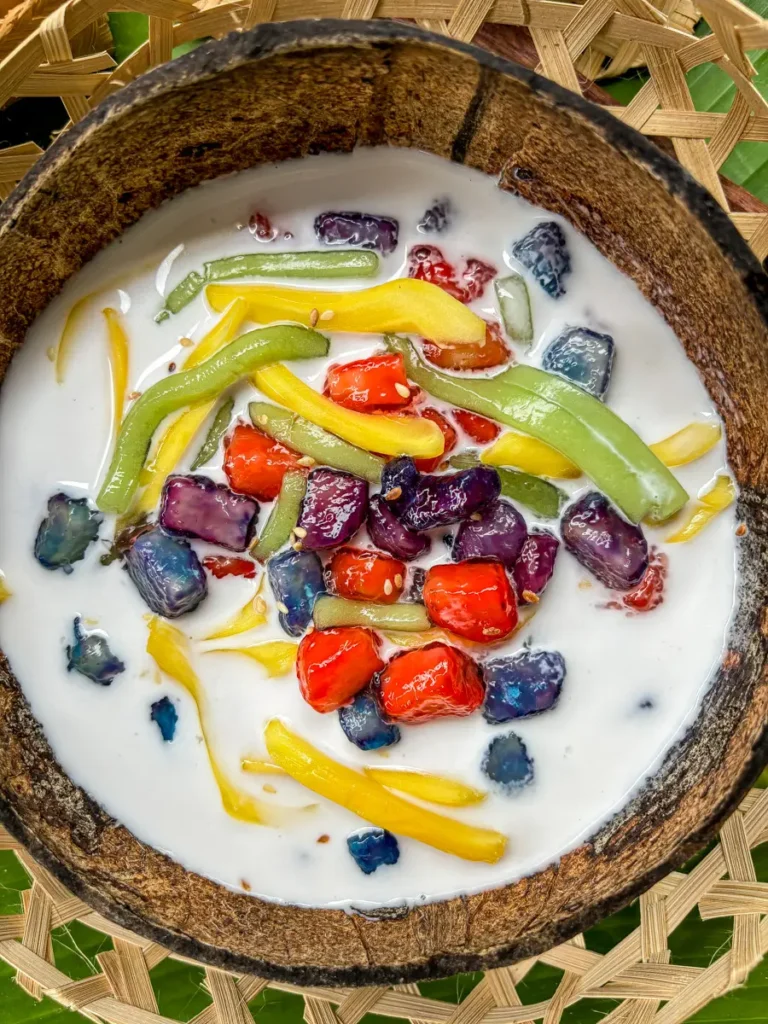 Close-up of Thai ruam mit with chewy tapioca pearls, sweet jackfruit strips, and jelly cubes in coconut milk, served in a coconut shell.