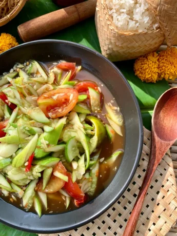 Spicy Lao cucumber salad in a dish with tomatoes and sticky rice on the side.