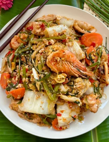 Suki hang, Thai sukiyaki stir-fry with shrimp, crisp vegetables, and glass noodles served in a white dish on a banana leaf.