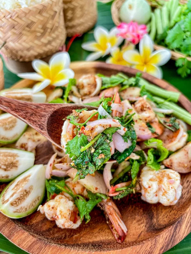 Close-up of Thai shrimp larb goong with mint, shallots, and chili, served in a wooden bowl.