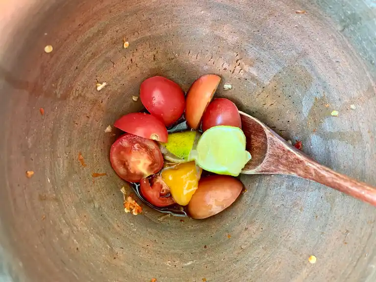 Ripe tomatoes, lime juice, lime peel, fish sauce, fermented fish sauce, and palm sugar in a mortar for spicy chili lime dressing.