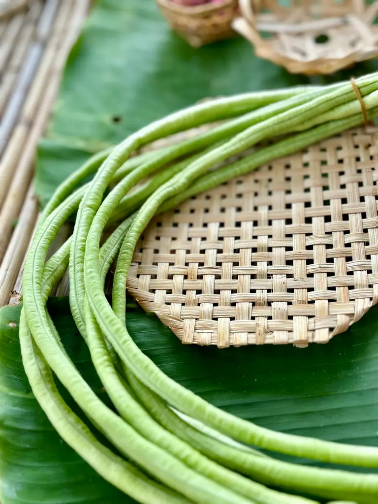 Fresh yard long beans on a woven bamboo mat, placed on a banana leaf.