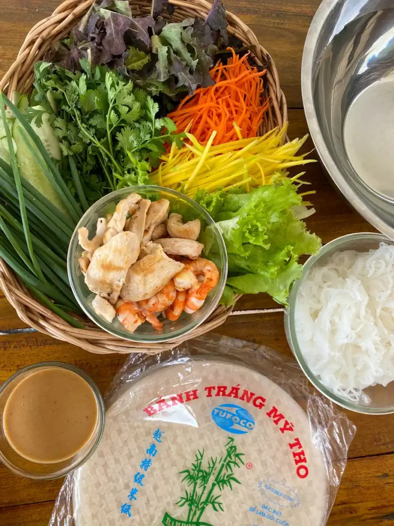 An assortment of fresh ingredients ready for making Thai shrimp rolls, including vegetables, rice vermicelli, and peanut sauce.