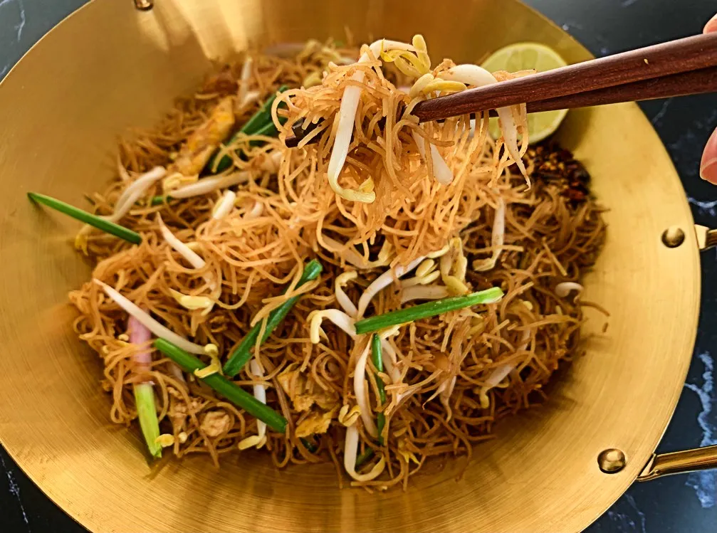 Close-up of delicious rice vermicelli noodles stir-fried with fresh vegetables, with chopsticks lifting some noodles.