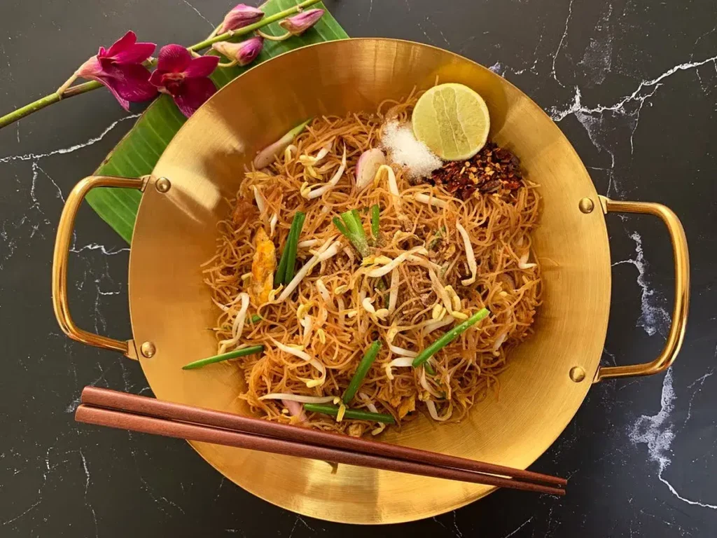 Golden wok of easy rice vermicelli stir-fry, garnished with lime and chili, ready to serve.