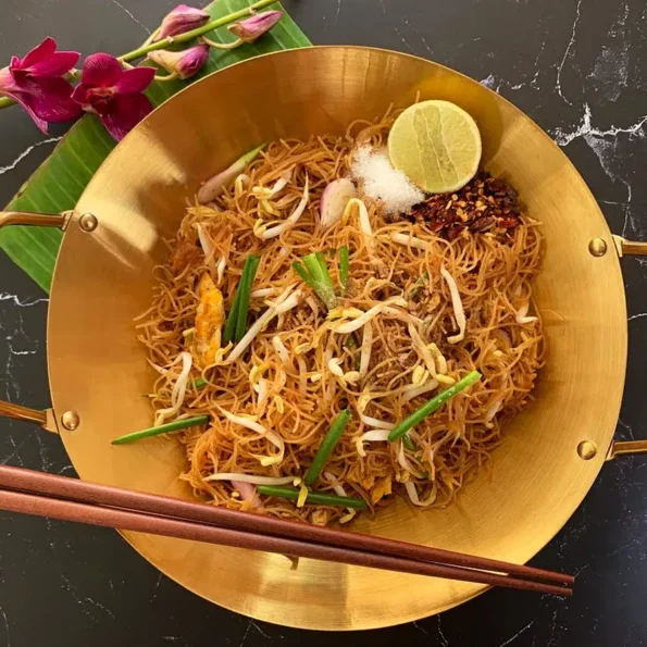 Golden wok of easy rice vermicelli stir-fry, garnished with lime and chili, ready to serve.