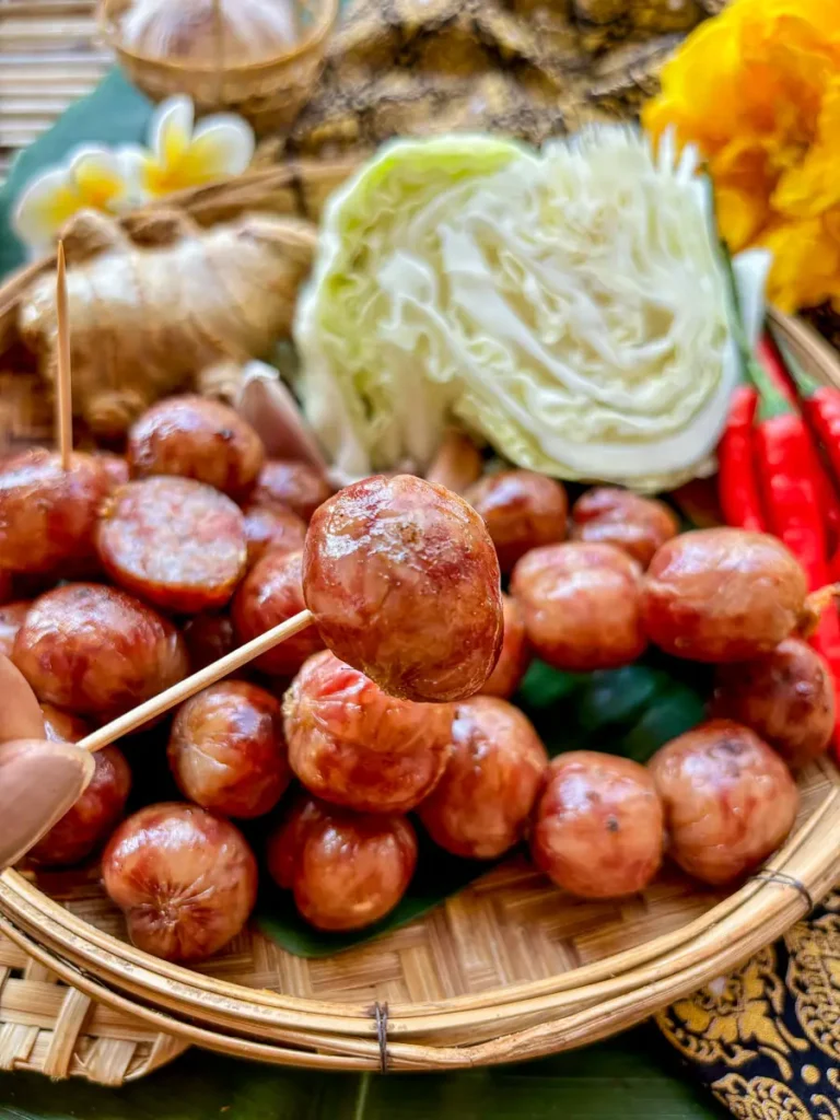 Sai krok Isan Thai sausages on a bamboo basket, with one sausage held in front of the camera.