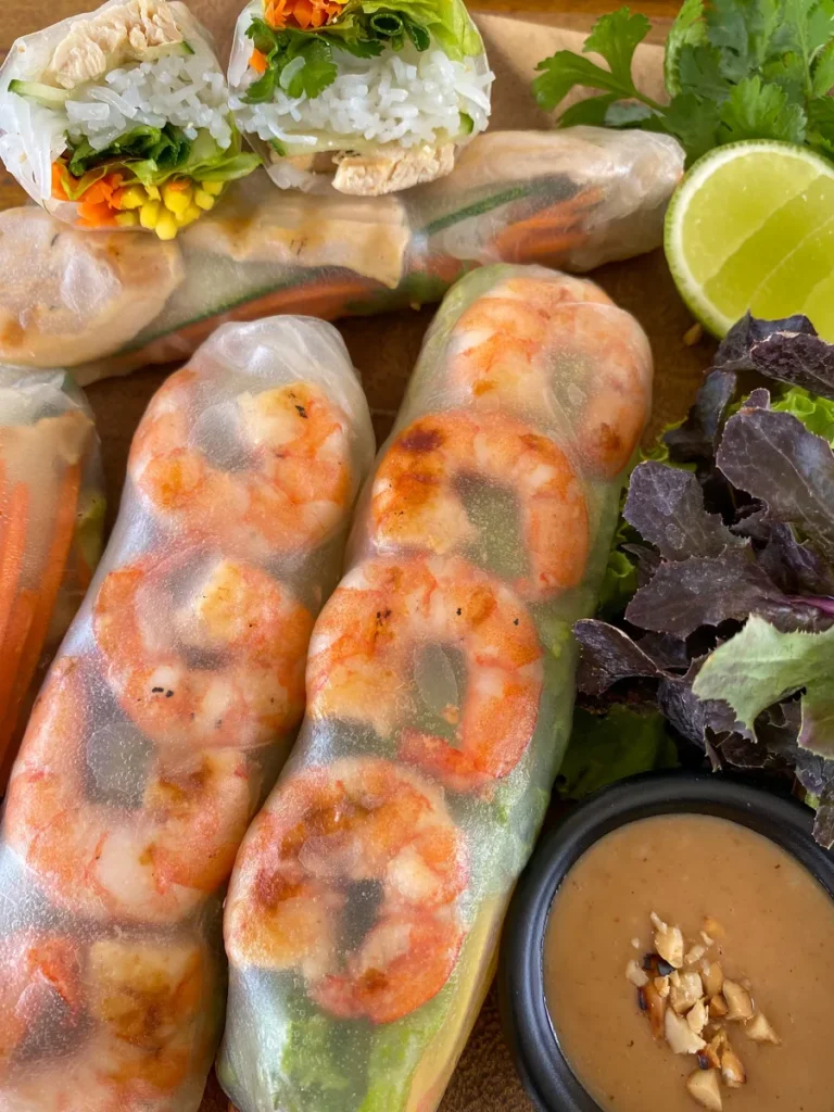 Close-up of Thai shrimp rolls with visible shrimp and fresh greens, served with peanut sauce on the side.