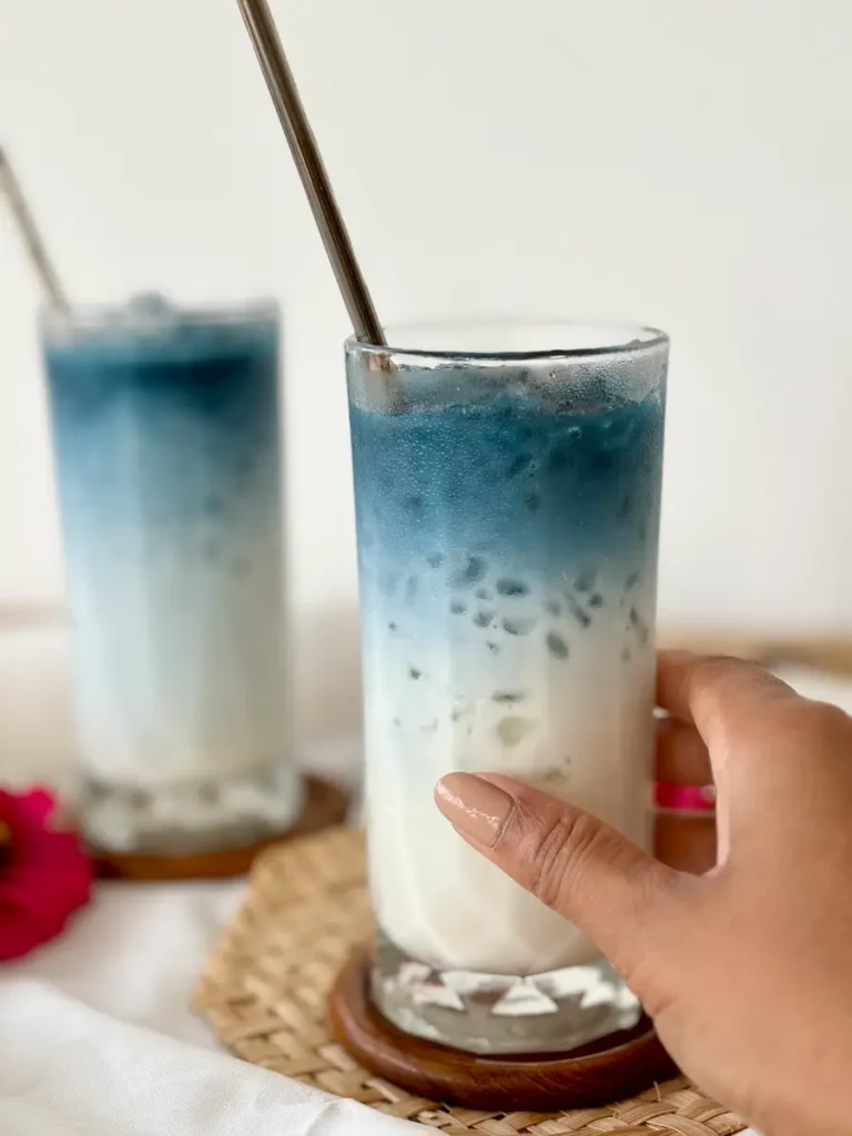 Close-up of a hand gently holding a glass of blue milk tea.