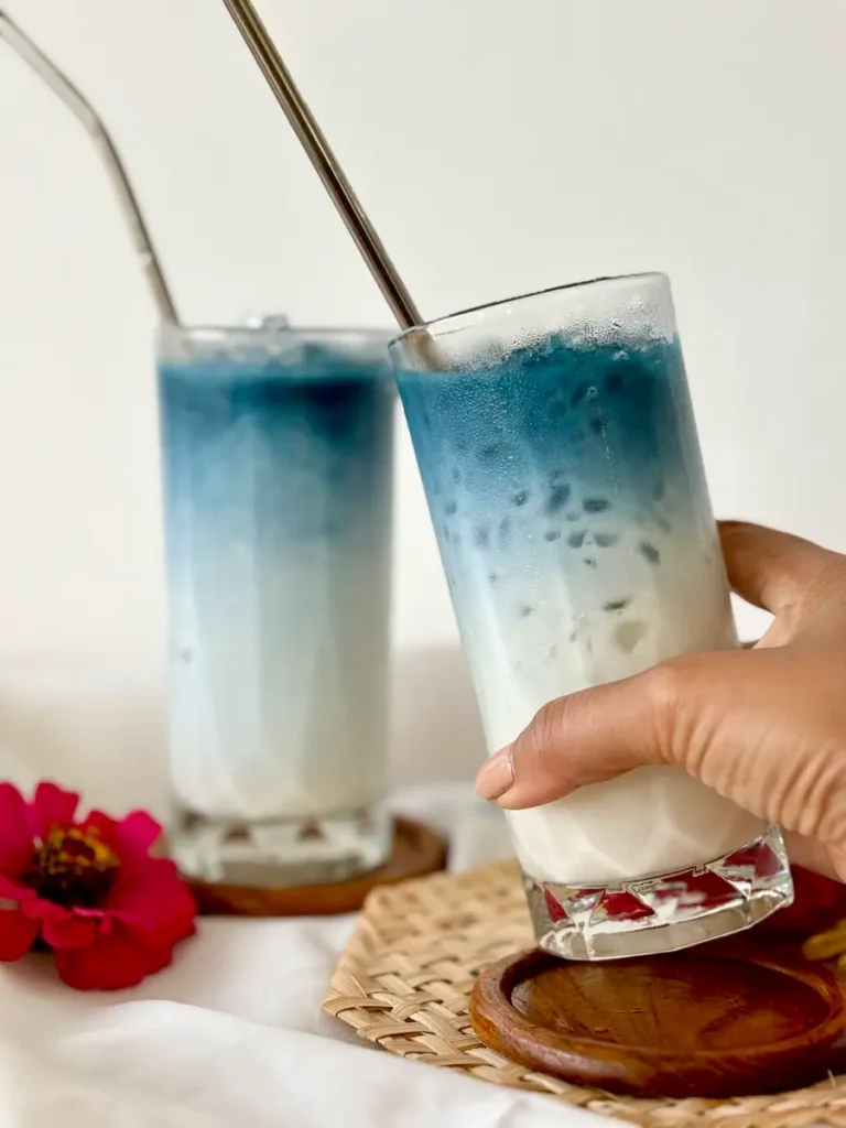 Hand holding tall glass of blue butterfly pea milk tea.