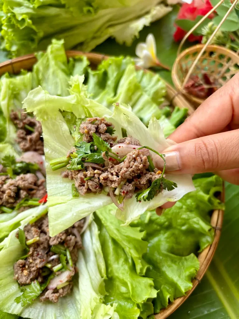 Hand holding a Thai chili beef lettuce wrap with fresh green herbs.