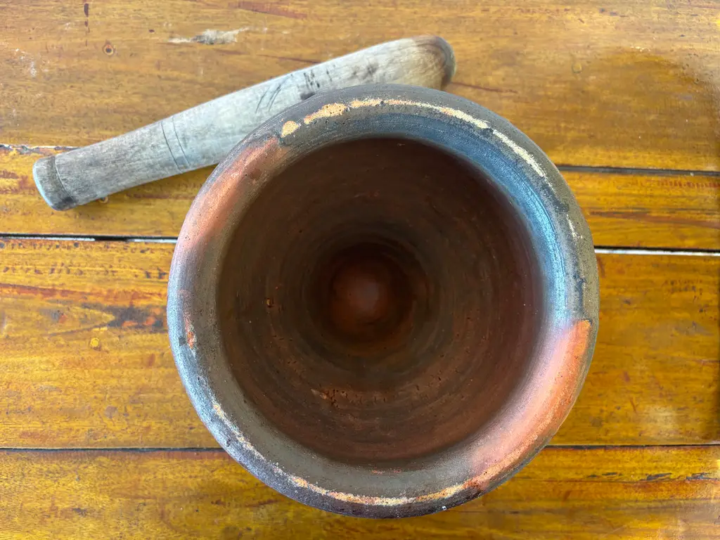 Close-up of a traditional Thai clay mortar and wooden pestle on a wooden background.