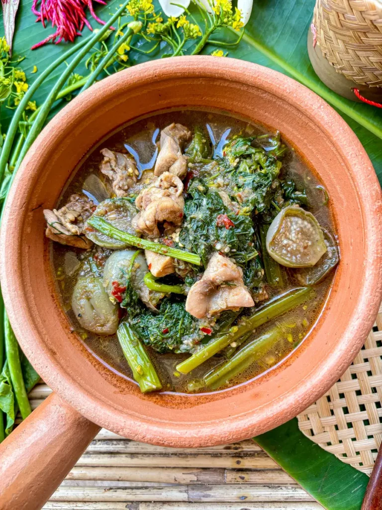 Gaeng om gai, a clear Thai chicken soup with Isan herbs, served on a banana leaf with sticky rice.