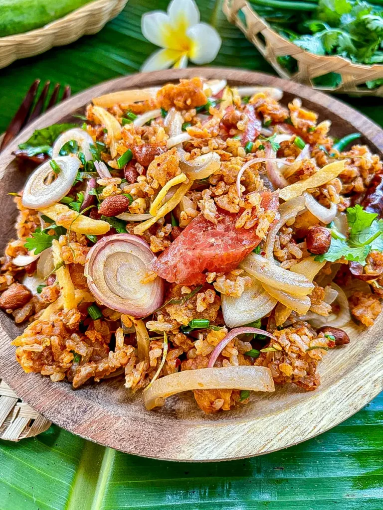 Close-up of nam khao tod, a Thai crispy rice salad recipe, with pork skin, fermented pork, fresh herbs, and spices.
