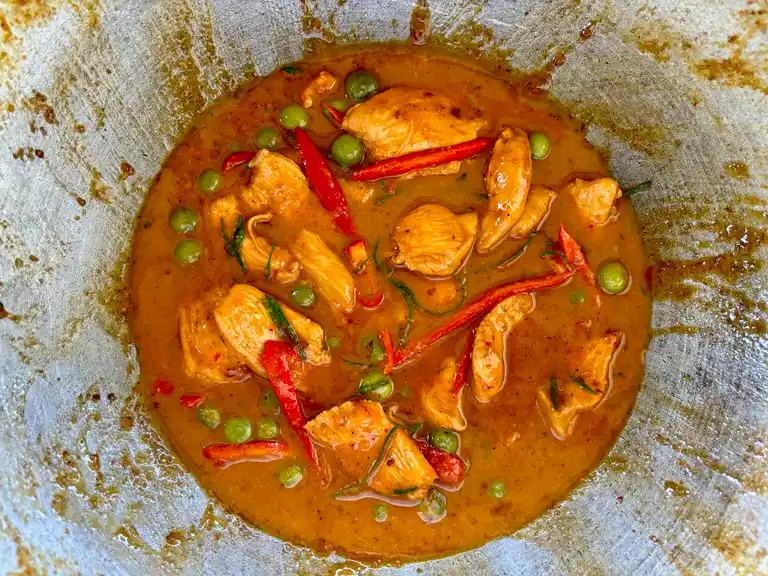 Gaeng panang chicken simmering in a wok with sliced red chili and green peas, ready to serve.
