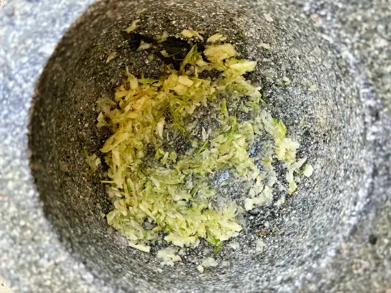 Garlic and coriander root being ground in stone mortar.