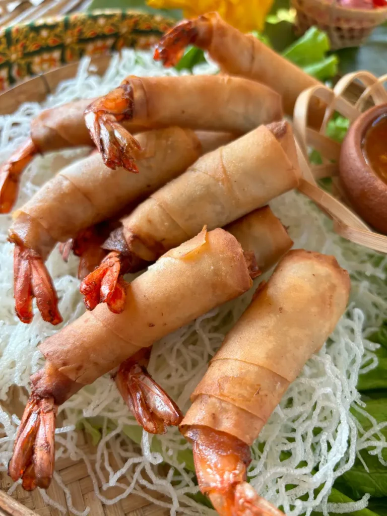 Close-up of goong hom pha, Thai shrimp rolls, with a side of sweet chili sauce.