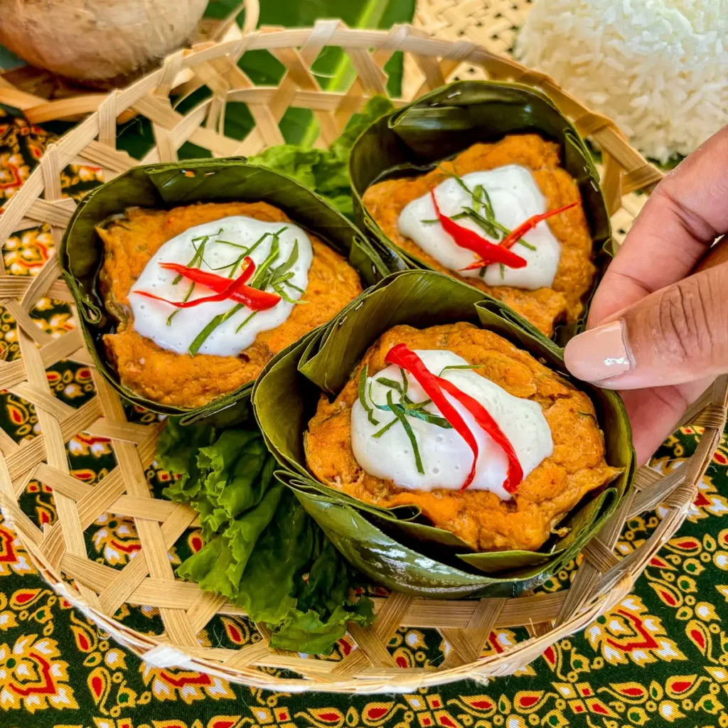 Thai hor mok pla steamed fish curry in banana leaf cups, topped with coconut cream, red chili, and kaffir lime.