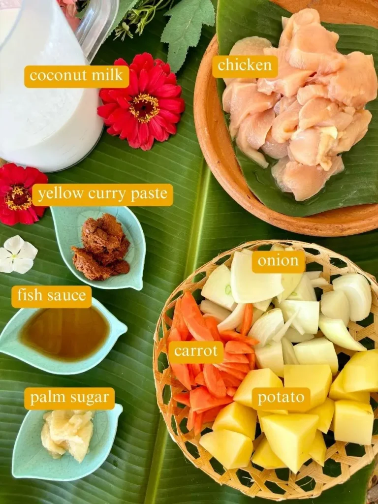 Top-view of ingredients for gang garee curry recipe: coconut milk, chicken, yellow curry paste, onion, fish sauce, carrot, potatoes, and palm sugar.