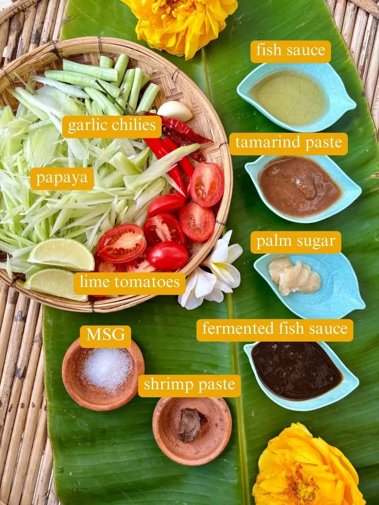 Ingredients for Lao papaya salad labeled: garlic, chilies, fish sauce, tamarind paste, palm sugar, MSG, fermented fish sauce, shrimp paste, lime, and tomatoes.