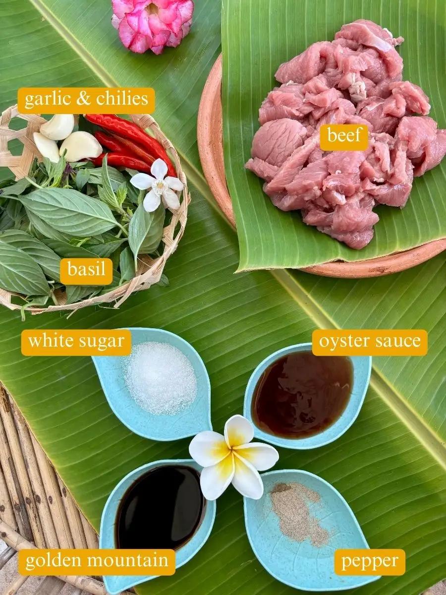 Pad horapa ingredients on banana leaf: garlic, chilies, basil, beef, sugar, oyster sauce, soy sauce, and pepper.
