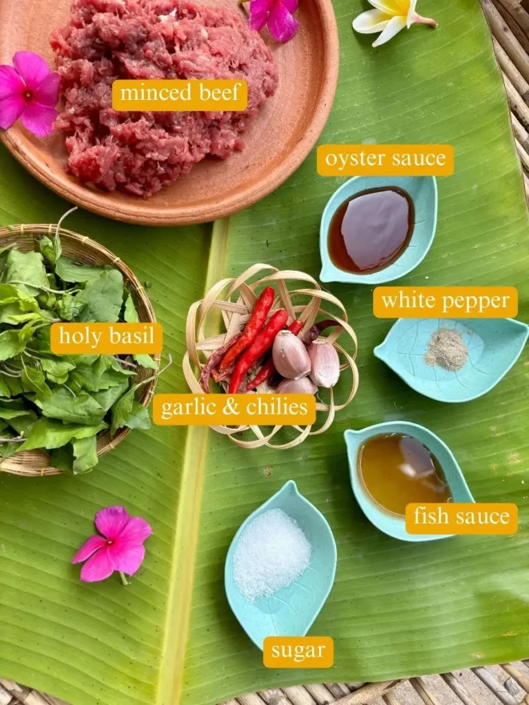 Top-view of ingredients for Thai basil beef recipe: minced beef, oyster sauce, white pepper, fish sauce, white sugar, garlic, chilies, and holy basil.