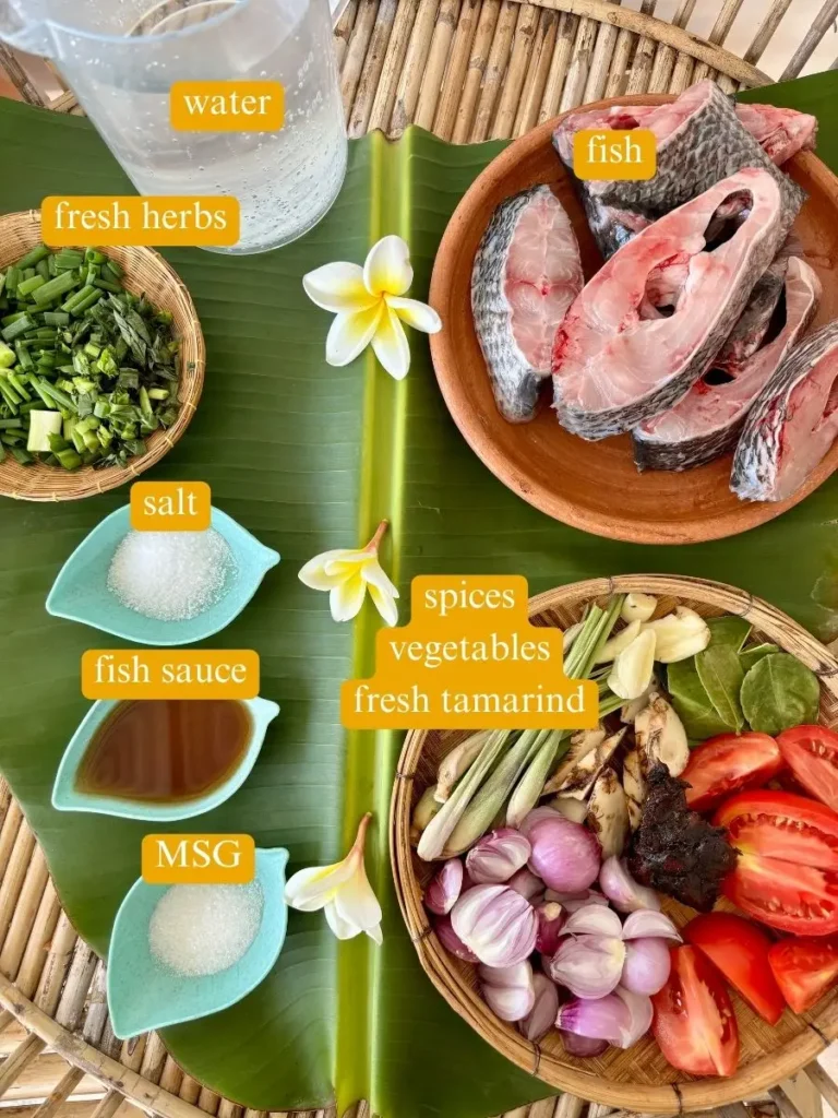 Ingredients for tom yum pla recipe including fish sauce, galangal, kaffir lime leaves, lemongrass, tomatoes, tamarind paste, and fresh herbs and spices.