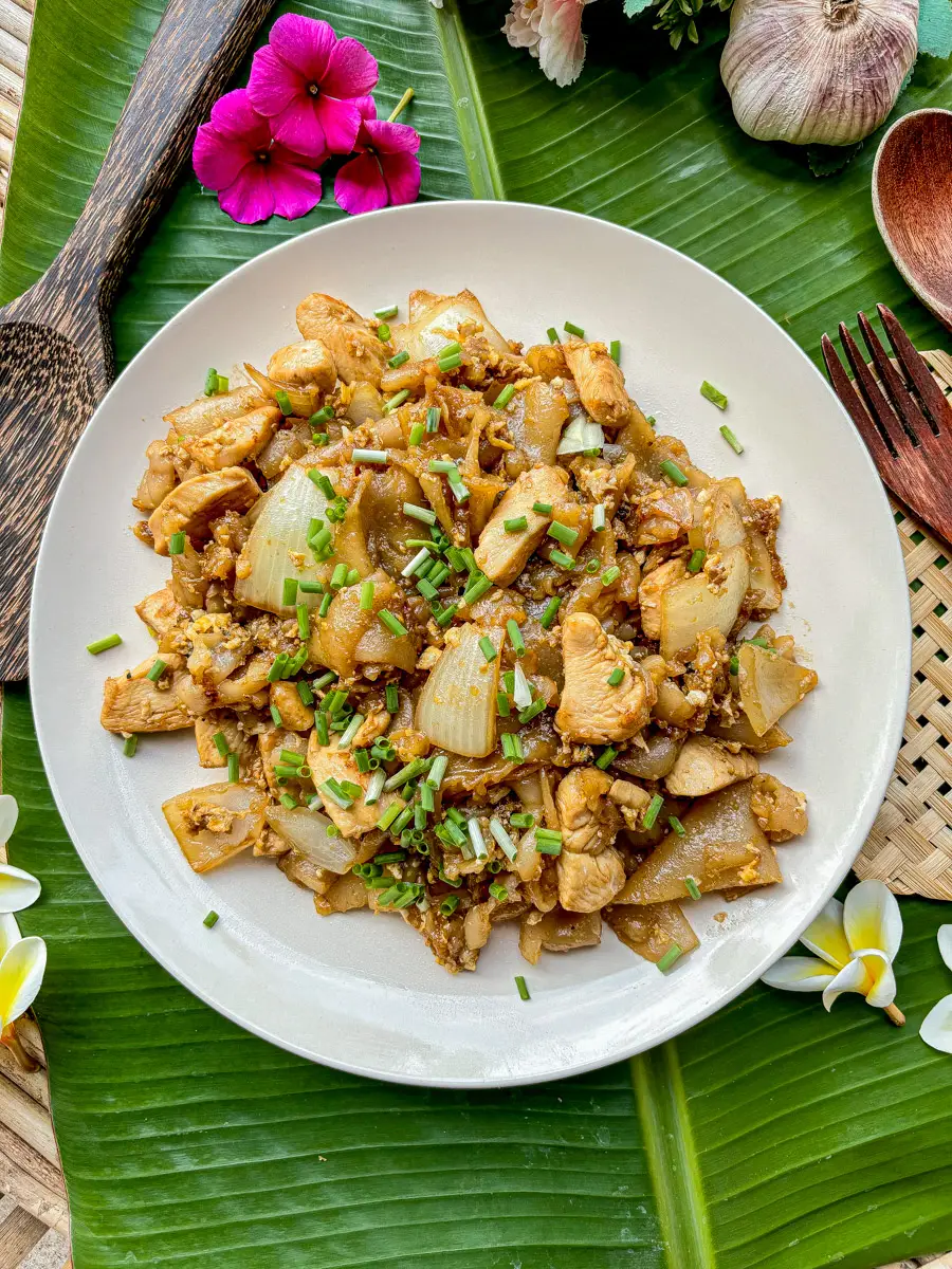 Thai kuay teow kua gai with wide rice noodles, chicken, egg, and onions garnished with chopped green onions.