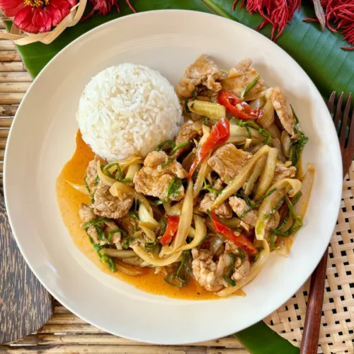 Thai moo pad prik pao, a spicy pork stir-fry, served with jasmine rice on a white plate, garnished with red chilies and green onions.