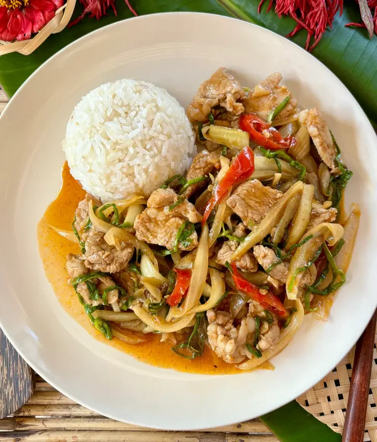 Thai moo pad prik pao, a spicy pork stir-fry, served with jasmine rice on a white plate, garnished with red chilies and green onions.