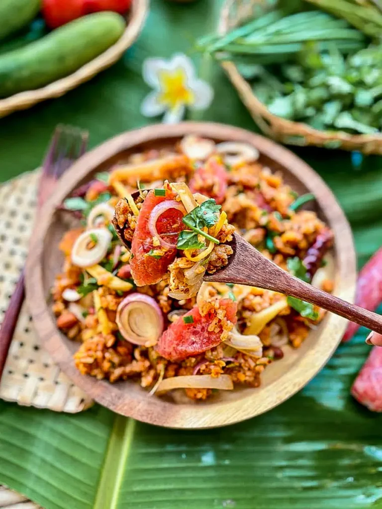 Close-up of crispy rice salad, nam khao tod with a fork lifting some of the salad over vegetables and fresh herbs.