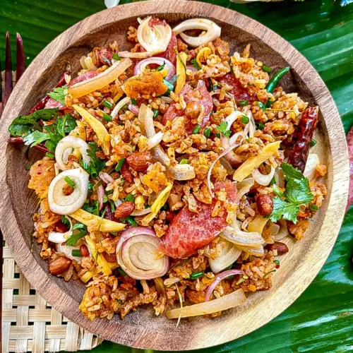 Nam khao tod Thai crispy rice salad with fresh herbs and sour sausage on a wooden plate over banana leaf.