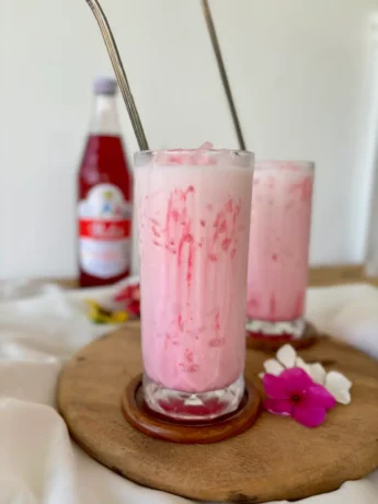 Creamy Thai Nom Yen pink milk in a tall glass, with streaks of Sala syrup.