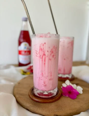 Creamy Thai Nom Yen pink milk in a tall glass, with streaks of Sala syrup.
