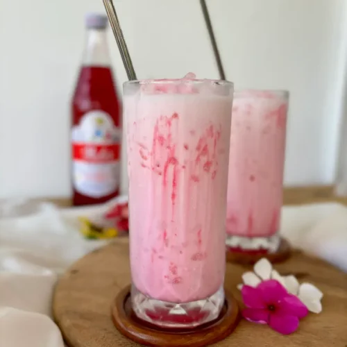 Creamy Thai Nom Yen pink milk in a tall glass, with streaks of Sala syrup.