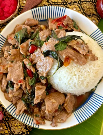 Pad horapa, a Thai sweet basil stir-fry with beef, served with jasmine rice on a traditional patterned cloth.