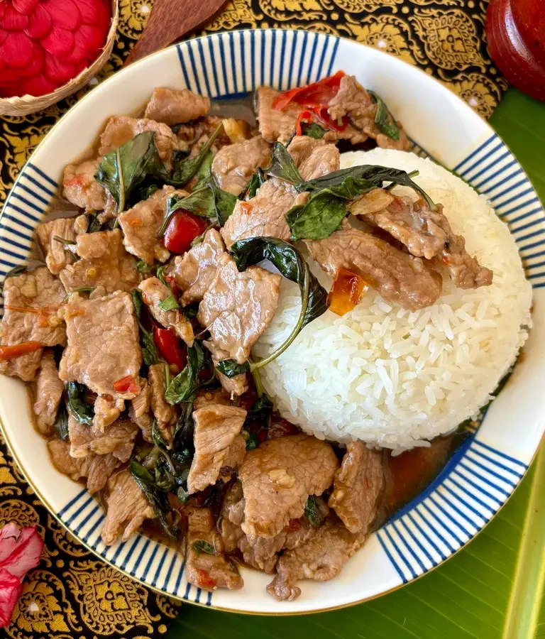 Pad horapa, a Thai sweet basil stir-fry with beef, served with jasmine rice on a traditional patterned cloth.