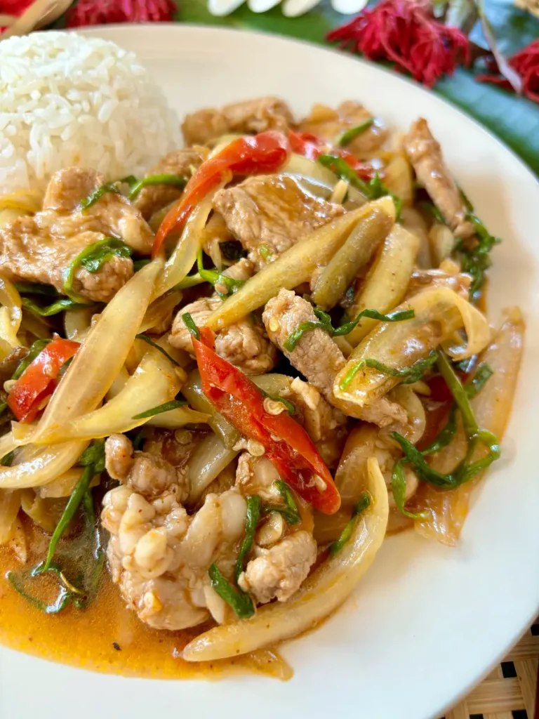 Pad prik pao pork stir-fried with vegetables and chilies, served with steamed jasmine rice in a white dish.