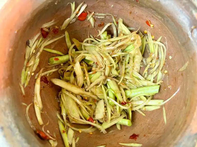 Green papaya shreds with salad dressing and chilies in mortar.