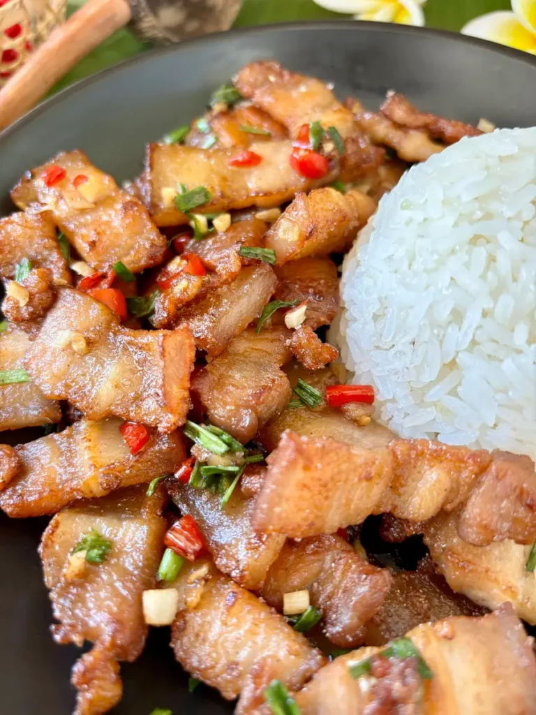 Pork belly chili garlic stir-fry garnished with green onions and chopped chilies, served with jasmine rice.