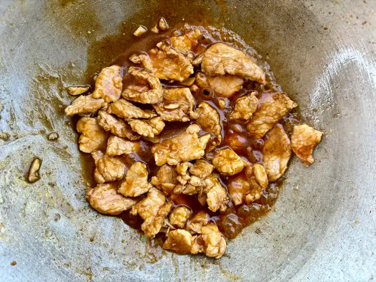 Pork pieces cooking in a rich, brown stir-fry sauce in a wok.