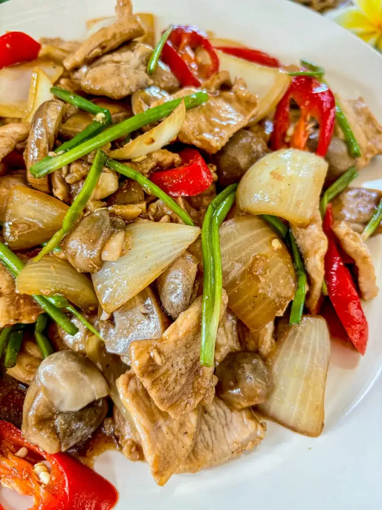 Close-up of pork in oyster sauce with mushrooms , onions, red chilies, and green onions on a white plate.