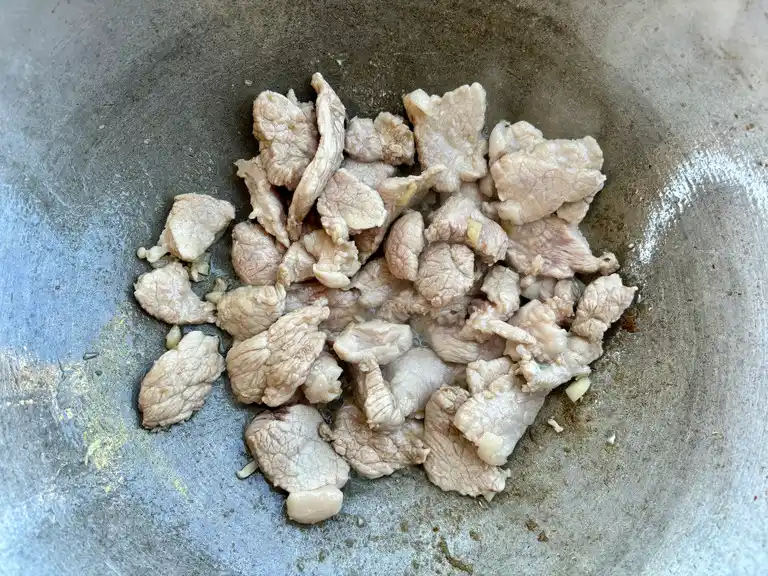 Raw pork strips cooking in a wok.