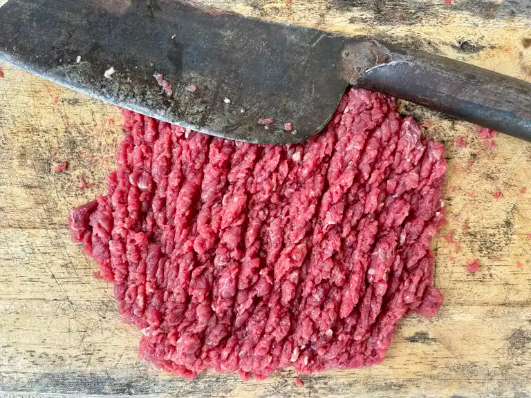 Raw minced beef on a wooden cutting board with a cleaver.