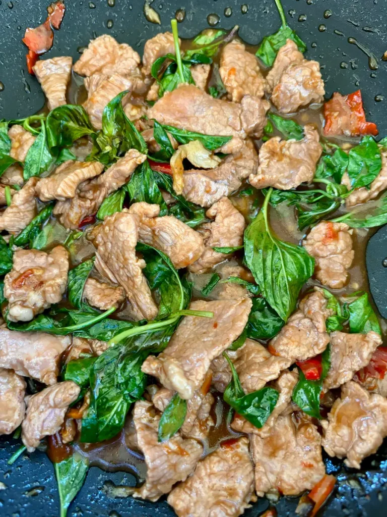 Thai basil beef stir-fry with greens in a sizzling wok.