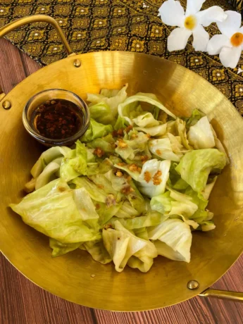 Golden wok filled with Thai cabbage stir-fry, garnished with fried garlic, served with chili oil on the side.